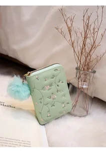 Close-up of mint green embroidered coin purse with pink flowers and a plush ball charm