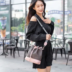 Sac seau marron avec bordure rose et bandoulière large dans un décor urbain moderne