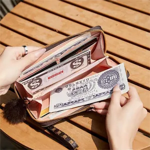 Women's long zip wallet with wristlet and plush charm shown in an outdoor lifestyle setting