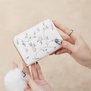 White faux leather mini wallet with pink floral embroidery and large white fur pompom