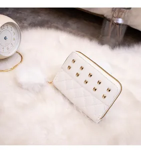 Detailed view of cream quilted purse with gold studs and a white faux fur pompom