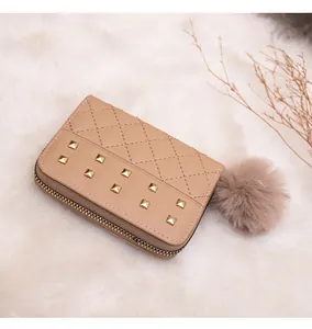 Detail of apricot quilted wallet featuring gold stud accents and a large plush pom-pom