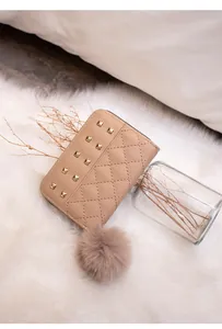 Detail of pink quilted wallet with gold studs and a fluffy pom-pom charm on soft rug