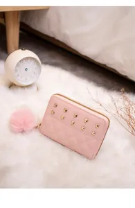 Detailed view of pink quilted wallet with gold studs and a fluffy pom-pom charm