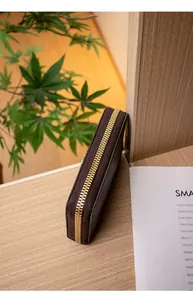 Dettaglio della pochette marrone scuro testurizzata con zip dorata su legno
