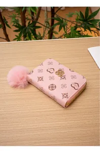 Vista dettagliata del portafoglio rosa floreale con pompon decorativo su legno