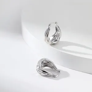 Détail de créoles argentées minimalistes en forme de goutte avec une texture martelée irrégulière