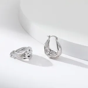 Détail de boucles d'oreilles créoles argentées avec texture irrégulière en métal liquide