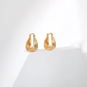 Gros plan sur des boucles d'oreilles créoles en laiton doré à texture ondulée