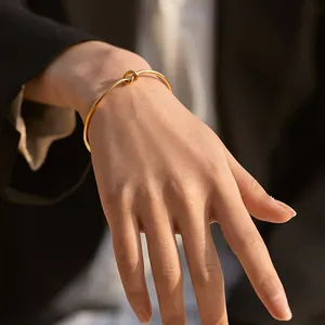Close-up of a minimalist 18K gold-plated brass knot bracelet worn with office attire