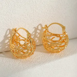 Close-up of golden hollow woven spherical earrings on a textured white display stand