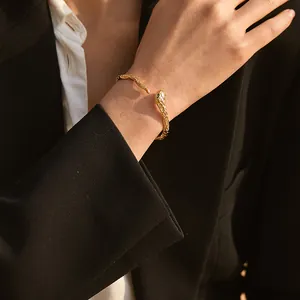 Detail of 18K gold plated brass snake bangle with green accents on model's wrist