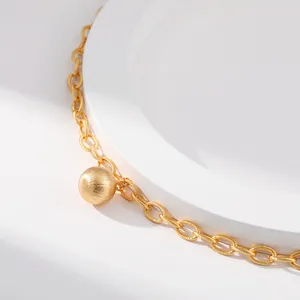 Makro-Detail einer 18K vergoldeten Messingkette mit einem gebürsteten Kugelanhänger