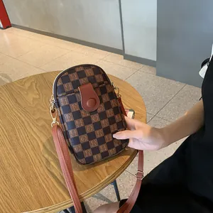 Brown checkered pattern mini crossbody phone bag with adjustable strap on wooden table