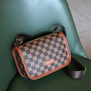 Bolso bandolera retro con patrón de cuadros y correa ancha sobre fondo de cuero verde