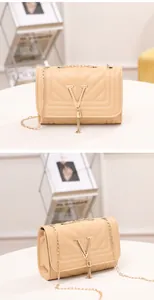 Detail view of beige quilted handbag with gold V-shaped logo, tassel and chain strap