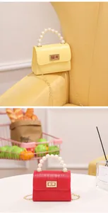 Detalle de mini bolso con patrón de cocodrilo, asa de perlas y correa de cadena dorada