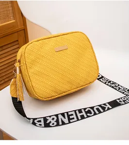 Detailed view of yellow woven crossbody bag with metal plaque and letter printed strap