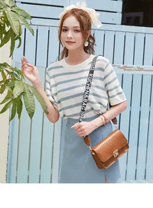 Detailed view of brown crossbody bag with woven flap, gold lock and striped strap