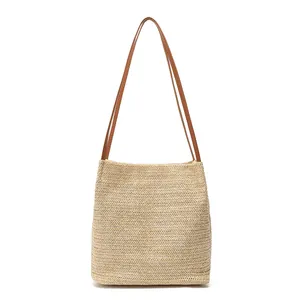 Handcrafted woven straw tote bag with brown leather shoulder straps on white background