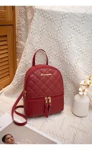 Detail of burgundy quilted leather backpack with gold logo and tassel on knit background