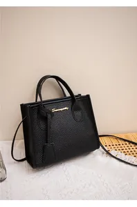 Dettaglio della pelle nera a grana di litchi e del logo in metallo dorato sulla borsa