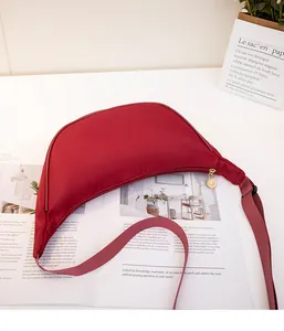 Detail of red nylon crescent crossbody bag placed on a magazine with chic decor
