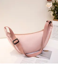 Detail of pink crescent crossbody bag with adjustable wide strap on a minimalist setup