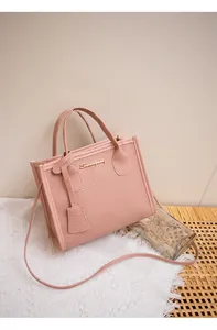 Dettaglio borsa a mano rosa con trama a grana e logo dorato su sfondo pizzo