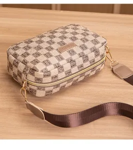 Detail view of the brown checkered crossbody bag with wide canvas strap and gold zipper