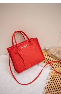 Dettaglio borsa rossa con trama litchi, logo dorato e sfondo in pizzo bianco