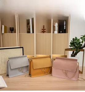 Chic suede crossbody bags in gray yellow and pink with gold rings on a wooden table