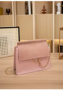 Detail of pink crossbody bag with suede flap and gold ring hardware on wood surface