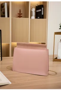 Close-up of pink flap square bag with gold metal chain strap on wooden surface