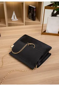 Detail shot of black PU crossbody bag with golden metal ring and chain on a wooden desk
