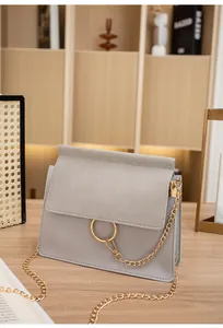 Detail of grey crossbody bag with gold ring hardware and chain strap on wooden table