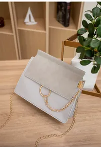 Detailed close-up of a two-tone crossbody bag with a large gold ring and chain on a desk