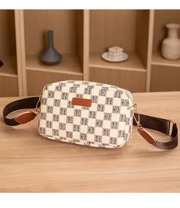 Detail showing the retro plaid fabric and leather brand logo on a small camera bag