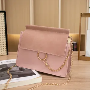 Elegant dusty pink crossbody square bag with gold ring and chain detail on wood table