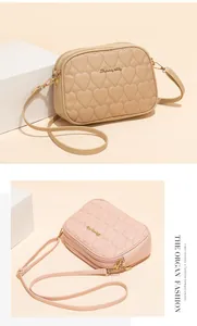 Detalle de costuras de corazón y cremalleras dobles en bolso bandolera beige de mujer