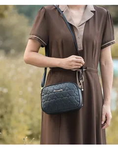 Detalle de bolso bandolera negro acolchado de corazón con logo dorado y cremallera