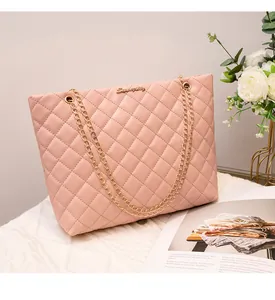 Détail du sac cabas matelassé rose clair avec chaînes dorées et logo en métal sur tissu
