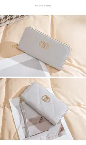 Close-up of light gray quilted long wallet with golden interlocking rings and wristlet