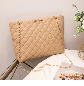 Détail d'un sac cabas matelassé beige avec chaîne dorée sur tissu en maille blanc