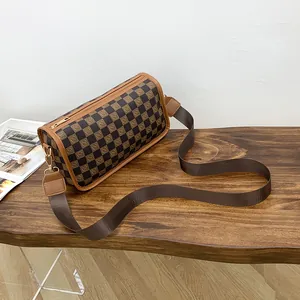Brown checkerboard barrel crossbody bag with wide strap on a textured wooden table