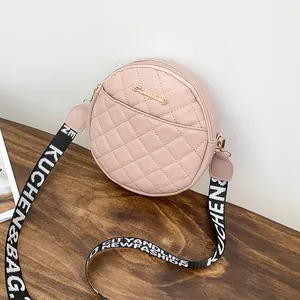 Sac bandoulière rond matelassé rose avec large sangle tissée sur bois sombre