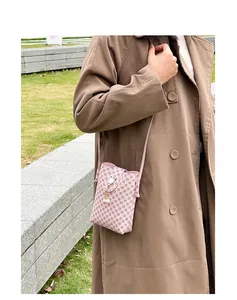 Close-up of pink printed crossbody phone bag with pearl pendant worn over a brown coat