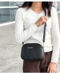 Detail view of black crossbody bag with V-quilted pattern and golden logo on a model