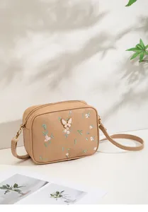 Detail of khaki crossbody bag featuring floral embroidery and gold butterfly hardware