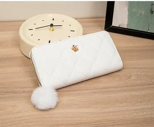 Detail of white quilted long wallet featuring gold floral hardware and a soft pom-pom